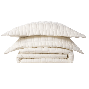 A folded, quilted, cream-colored bedding set comprising a comforter and two matching pillowcases with a grid pattern.