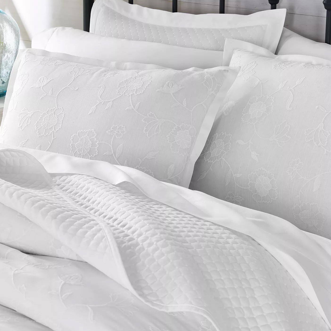 White bedding set featuring floral-patterned pillowcases with an embossed texture and a quilted blanket.