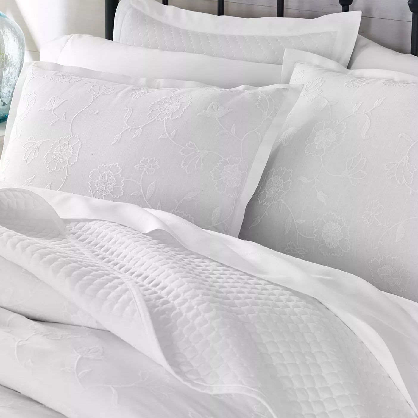 White bedding set featuring floral-patterned pillowcases with an embossed texture and a quilted blanket.