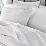 White bedding set featuring floral-patterned pillowcases with an embossed texture and a quilted blanket.