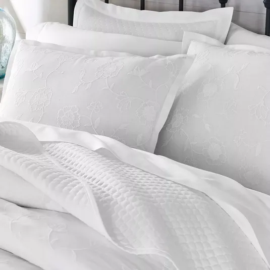 White bedding set featuring floral-patterned pillowcases with an embossed texture and a quilted blanket.