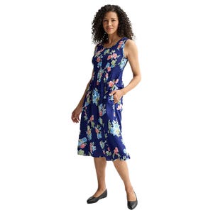 A woman is wearing a sleeveless navy blue floral dress with pink and blue flowers, paired with black flat shoes.