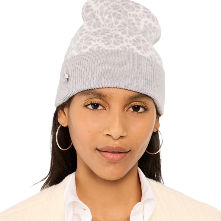 A woman wearing a light gray knit beanie with a white patterned top, paired with large hoop earrings and a white shirt with a blazer.