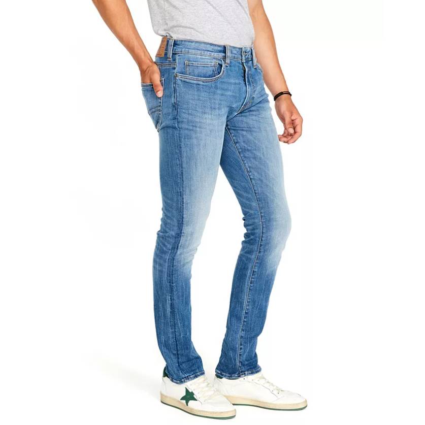 Light blue stretch-fit jeans with a slim, tapered leg design, worn with a casual grey t-shirt. The denim has a slightly faded look, with classic five-pocket styling and stitching details. Paired with white sneakers featuring green star accents.