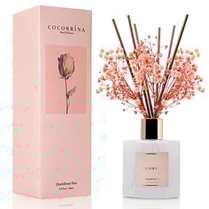 Cocorrína reed diffuser in a Sandalwood Rose scent, featuring a bottle with decorative reeds and small pink flowers, alongside its matching pink packaging.