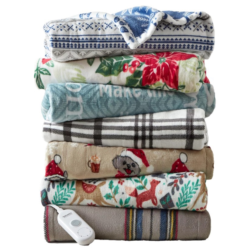A stack of colorful folded blankets featuring various patterns, including holiday themes and plaid, with an electric blanket controller visible at the bottom.