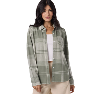 A woman is wearing a green and gray plaid long-sleeve button-up shirt with a chest pocket, paired with beige pants and a white top underneath.
