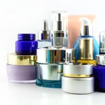 A variety of skincare packaging, including jars and bottles with shiny metallic lids and dispensers, in blue, purple, and gold colors.