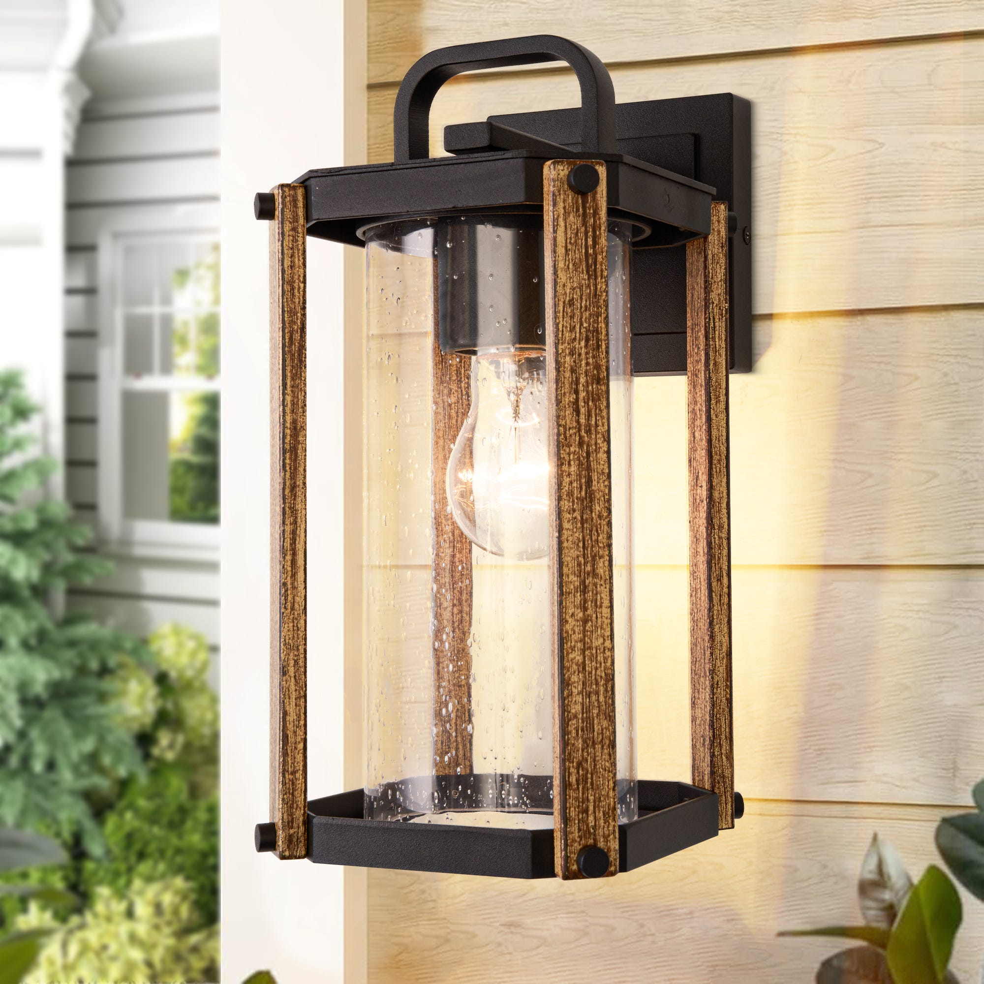 An outdoor wall-mounted lantern with a rustic design, featuring a clear glass cylinder and faux wood finish.
