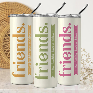 Three insulated tumblers with metal straws feature the word \“friends\“ in different colors: orange, green, and pink. Each has the phrase \“true friendship knows no distance.\“