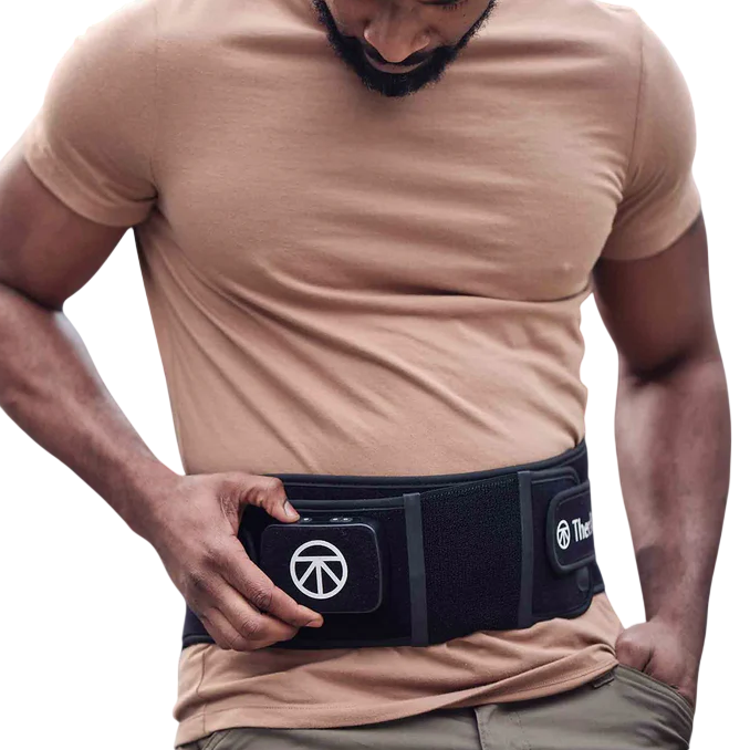 A person is adjusting a black wearable belt with a company logo, designed for back support or muscle recovery, over a beige shirt.