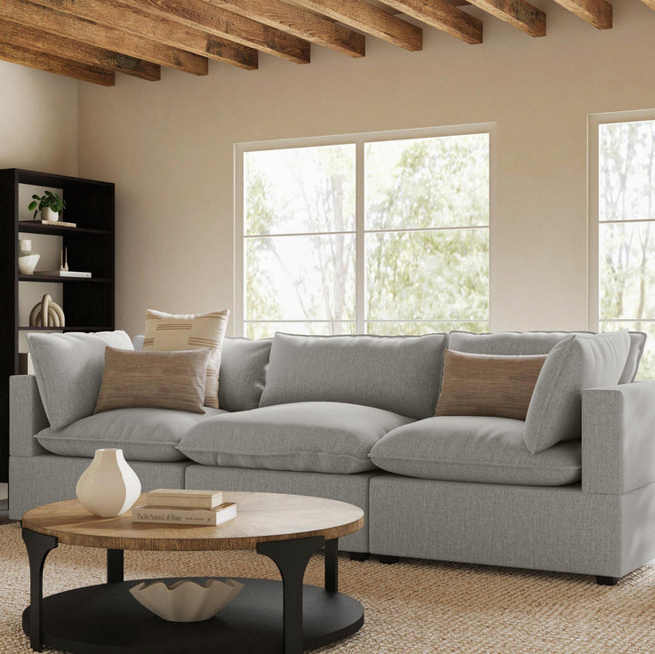 A gray sectional sofa, round wooden coffee table with black legs, and a dark bookshelf.