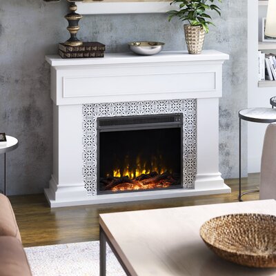 A white electric fireplace with a decorative tile-like surround and a mantel above, displaying a plant and decorative items, set against a grey wall.