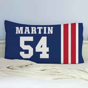 Blue pillowcase with \“MARTIN\“ and the number \“54\“ in white, alongside three vertical red stripes. The pillow rests on a white bed with a cream blanket.