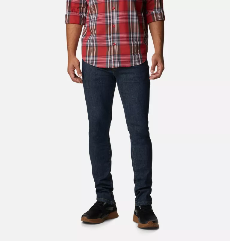 A person dressed in a red checkered shirt, dark blue jeans, and black shoes with brown soles.
