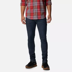 A person dressed in a red checkered shirt, dark blue jeans, and black shoes with brown soles.