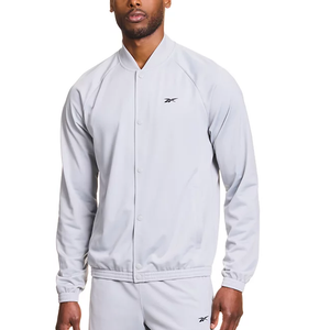 A person is wearing a light gray Reebok track jacket with a small logo on the chest, paired with matching track pants.