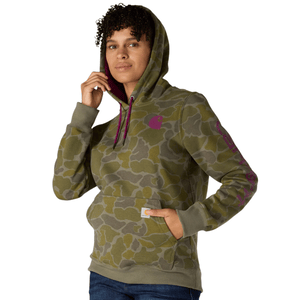 A person wears a green camouflage-patterned hoodie with purple accents, including a logo on the chest and sleeve. The hoodie has a front pocket and is paired with blue jeans.