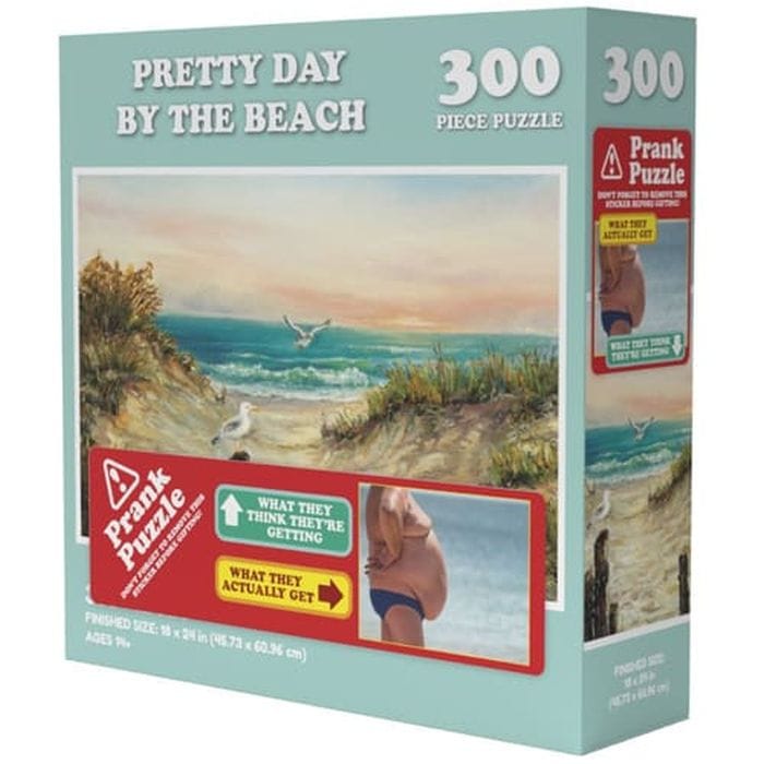 \“Pretty Day by the Beach\“ is a 300-piece prank puzzle with a deceptive cover showing a scenic beach, but inside is a different humorous image of a man's torso. Suitable for ages 9 and up, finished size is 18 x 24 inches.