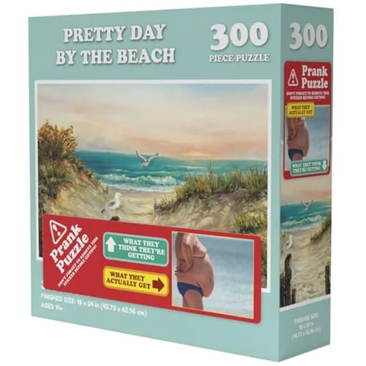 \“Pretty Day by the Beach\“ is a 300-piece prank puzzle with a deceptive cover showing a scenic beach, but inside is a different humorous image of a man's torso. Suitable for ages 9 and up, finished size is 18 x 24 inches.