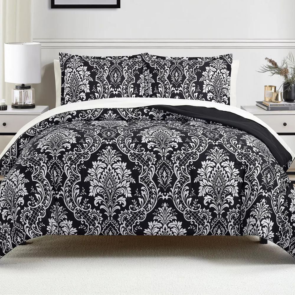 A bed features a black and white damask-patterned comforter and pillow shams, set in a contemporary bedroom with white side tables, lamps, and decorative elements.