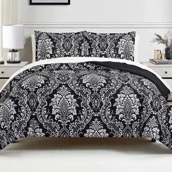 A bed features a black and white damask-patterned comforter and pillow shams, set in a contemporary bedroom with white side tables, lamps, and decorative elements.