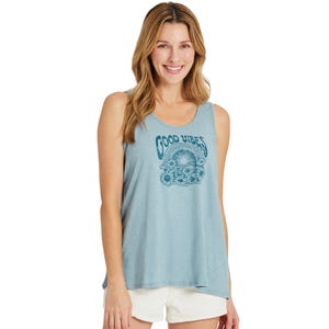 A woman is wearing a light blue sleeveless top with a \“Good Vibes\“ graphic and white shorts. She has long, wavy hair and is smiling.