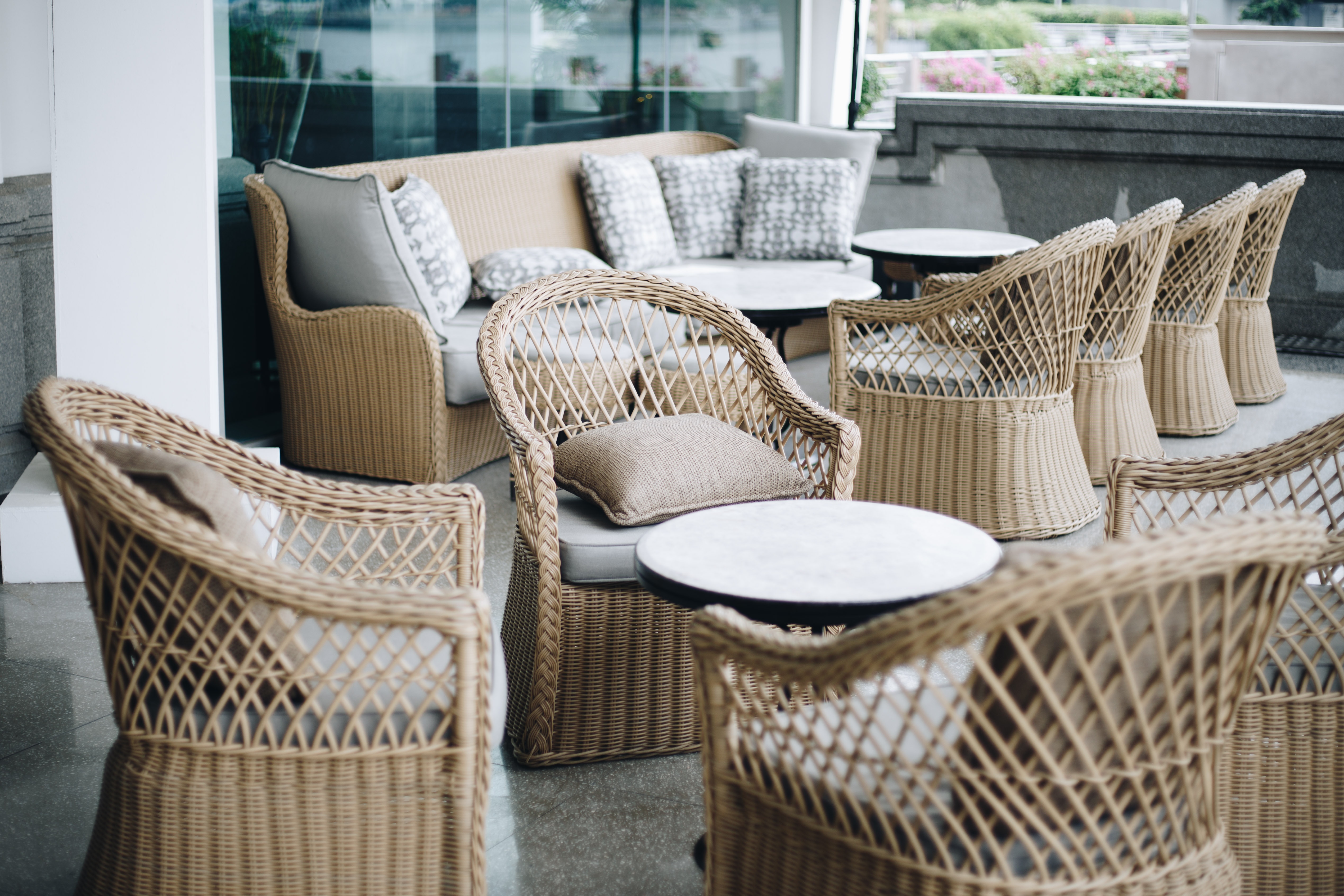 Outdoor wicker furniture including chairs with cushions and a sofa with a small round table.