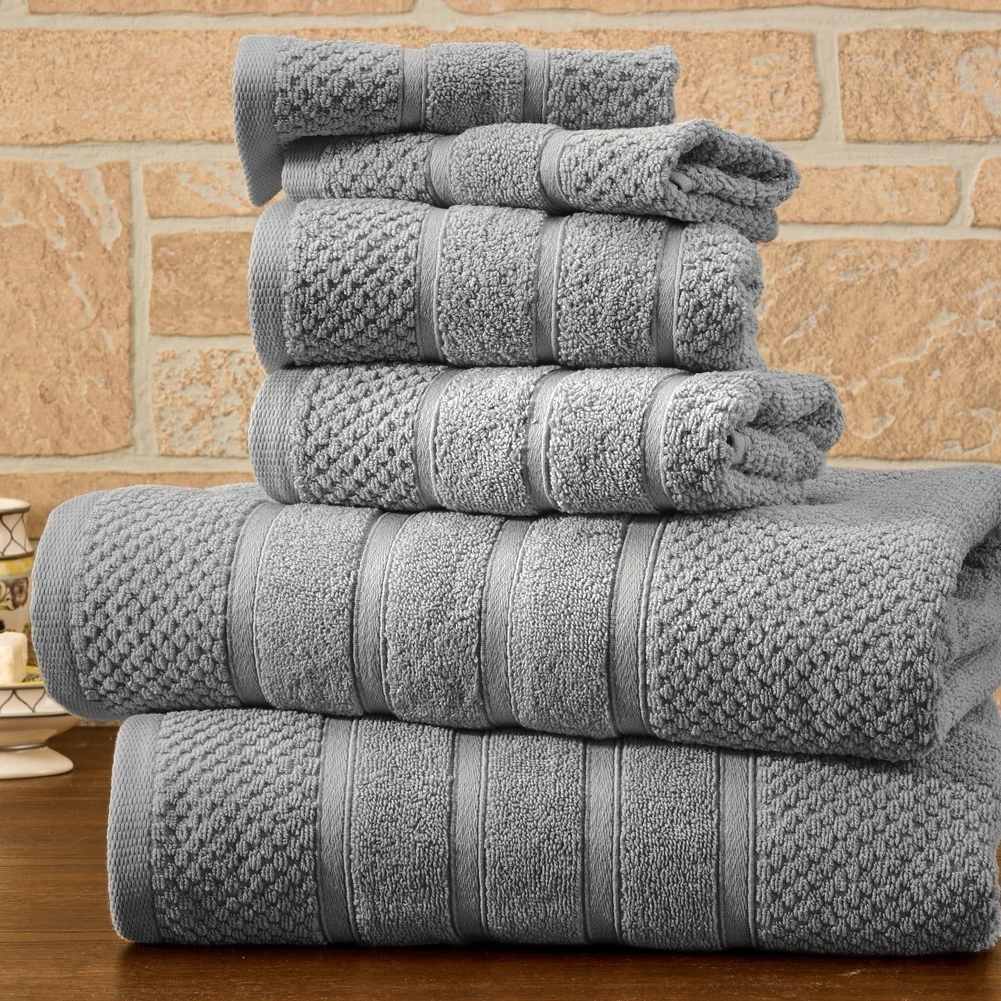 Stacked gray bath towels on a wooden surface against a stone wall.