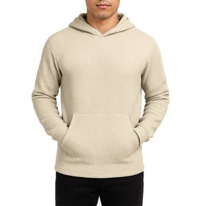 A beige, waffle-knit hoodie with a front pocket and long sleeves, paired with black pants.