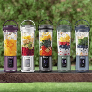 Five portable blenders in various colors, each filled with a mix of fruits and ingredients, displayed outdoors.