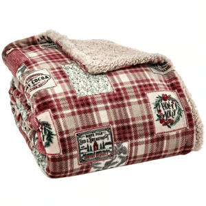 A plaid sherpa throw blanket featuring holiday-themed patches with designs like \“Hot Cocoa\“ and \“Holly Jolly\“.