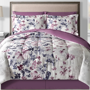 8-piece comforter set featuring a floral design with purple and pink tones, including a comforter, matching shams, bed skirt, and additional decorative pillows. The bedding has a soft blend of colors on a light background, complemented by a purple underside and skirt.