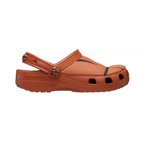 An orange slip-on clog featuring basketball-themed accents, including basketball patterns on the strap and side buttons, with ventilation holes and a strap at the back for support.