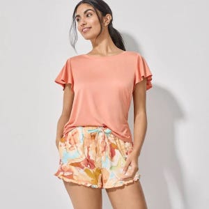 A woman is wearing a peach short-sleeved top paired with floral print shorts.
