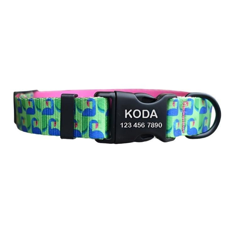 A colorful dog collar with a pattern of blue and green designs on a light background. It features a black buckle engraved with the name \“Koda\“ and a phone number.