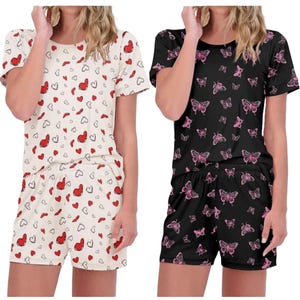 Two sets of short-sleeve pajama outfits; one with a cream background featuring red and black hearts, the other with a black background showcasing pink butterflies.
