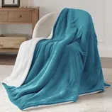 A plush blue throw blanket with a white sherpa lining draped over a cream-colored chair. In the background, there's a wooden side table with a basket underneath.