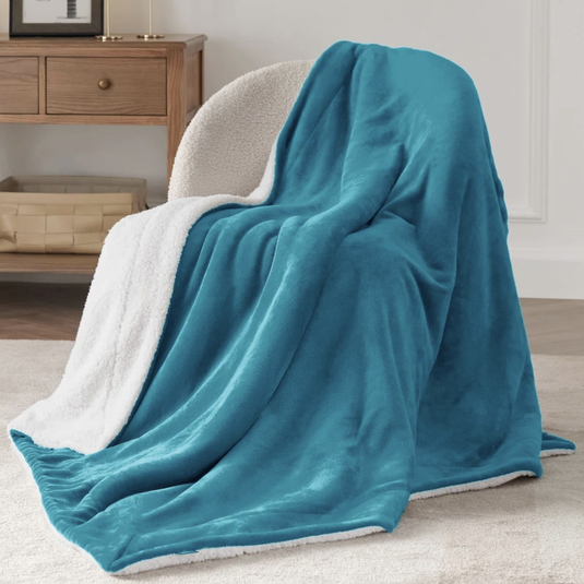 A plush blue throw blanket with a white sherpa lining draped over a cream-colored chair. In the background, there's a wooden side table with a basket underneath.