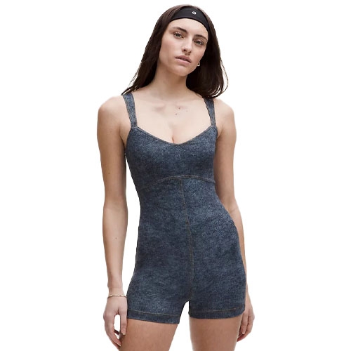 A person wearing a blue denim-look one-piece romper with thick straps and a black headband.