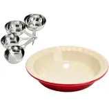 A set of stainless steel measuring cups is next to a red and cream ceramic pie dish with a scalloped edge.