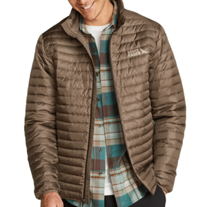 Eddie Bauer Microlight Down Jacket is a lightweight, quilted jacket in brown. It features a front zipper, branded logo on the chest, and is layered over a plaid shirt and a white tee.