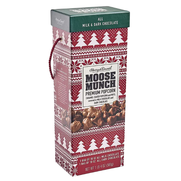 Harry & David Moose Munch Premium Popcorn features caramel-coated popcorn and nuts covered in milk chocolate and dark chocolate. The package contains two 10 oz bags, one of each chocolate type, and has a festive red design with white trees.