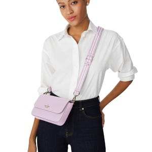 A woman wears a Kate Spade crossbody with pouch in light purple, featuring a structured design, flap closure, and an adjustable strap. She pairs it with a white shirt and dark jeans, showcasing a casual, elegant look.