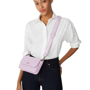 A woman wears a Kate Spade crossbody with pouch in light purple, featuring a structured design, flap closure, and an adjustable strap. She pairs it with a white shirt and dark jeans, showcasing a casual, elegant look.