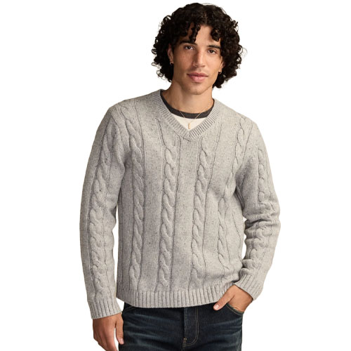 A man is wearing a light gray cable-knit V-neck sweater over a dark gray T-shirt with blue jeans.