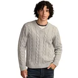 A man is wearing a light gray cable-knit V-neck sweater over a dark gray T-shirt with blue jeans.