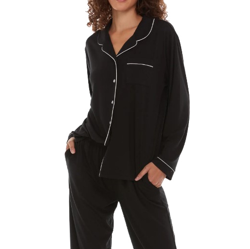 A woman is wearing a black Flora Nikrooz pajama set with white piping details along the edges, featuring a long-sleeve button-up top and matching pants.