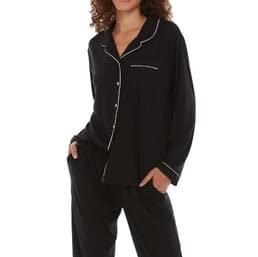 A woman is wearing a black Flora Nikrooz pajama set with white piping details along the edges, featuring a long-sleeve button-up top and matching pants.