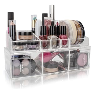 Clear acrylic makeup organizer with compartments holding lipsticks, nail polishes, eyeshadow palettes, lip gloss, foundation jars, and blush.